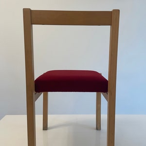 May include: A wooden chair with a red upholstered seat. The chair has a simple design with straight lines and a rectangular back.