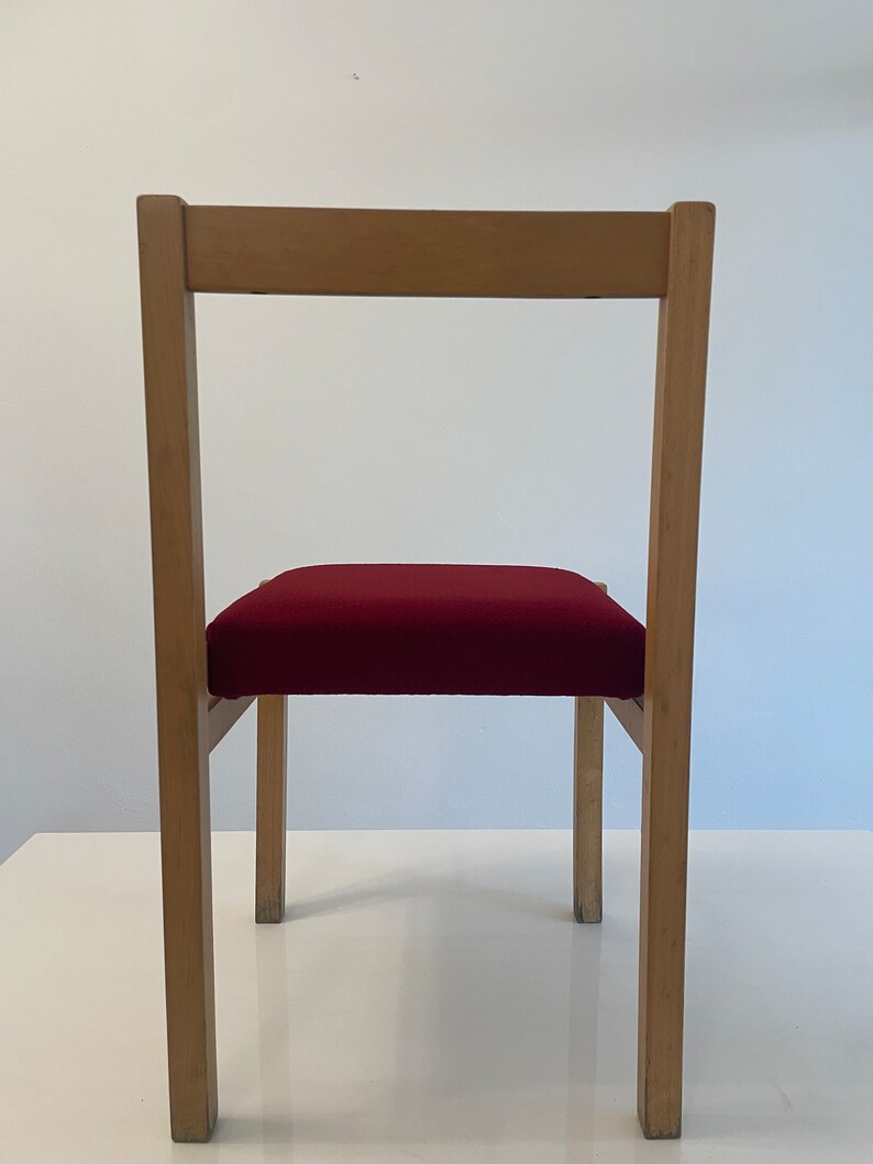 May include: A wooden chair with a red upholstered seat. The chair has a simple design with straight lines and a rectangular back.