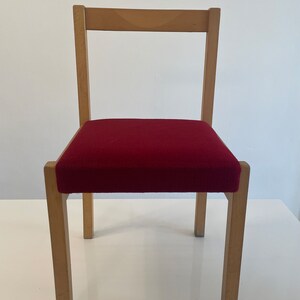 May include: A simple wooden chair with a red upholstered seat. The chair has a rectangular back and four legs.
