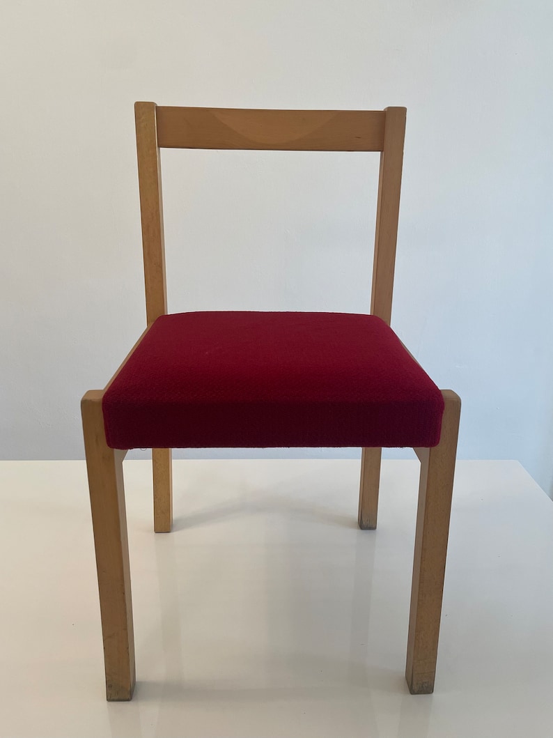 May include: A simple wooden chair with a red upholstered seat. The chair has a rectangular back and four legs.