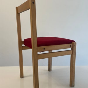 May include: A wooden chair with a red upholstered seat. The chair has a simple design with straight lines and a rectangular seat.