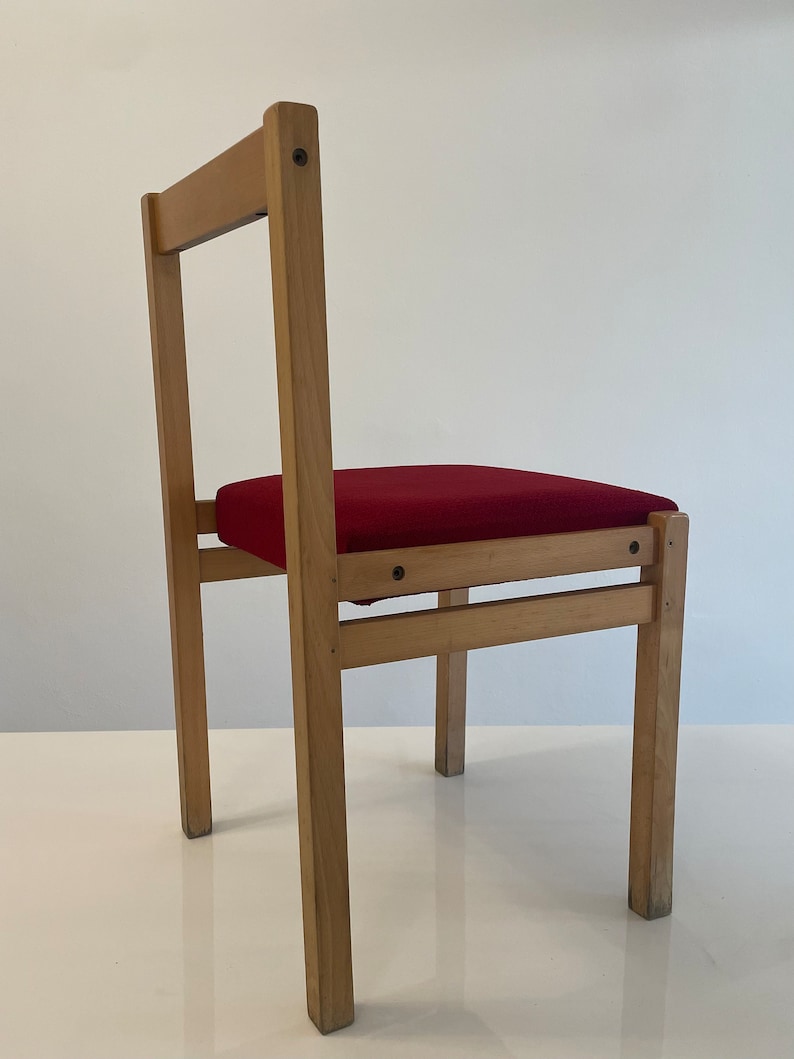 May include: A wooden chair with a red upholstered seat. The chair has a simple design with straight lines and a rectangular seat.