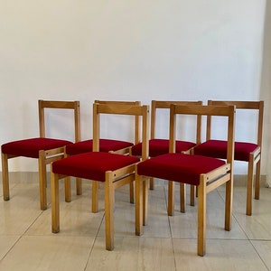 May include: Six wooden chairs with red fabric seats. The chairs have a simple, mid-century modern design.