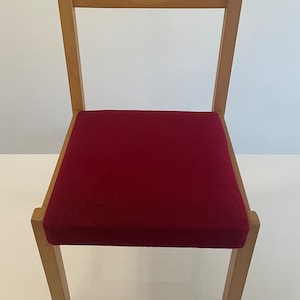 May include: A wooden chair with a red upholstered seat. The chair has a simple design with straight lines and a rectangular seat.
