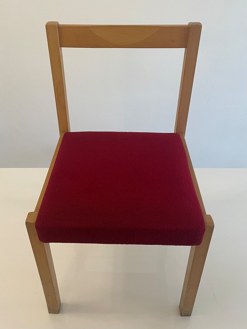 May include: A wooden chair with a red upholstered seat. The chair has a simple design with straight lines and a rectangular seat.