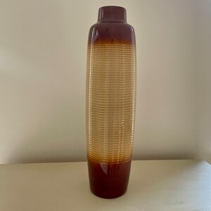 May include: A tall, decorative vase with a brown and tan color scheme. The top and bottom sections are brown, while the middle section features a ribbed, tan design. The vase has a slender, elongated shape, suitable for home decor.