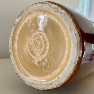 May include: A brown ceramic jug with a glossy finish. The base is light tan with a white rim and a stamped design. The jug's exterior is a deep brown color.
