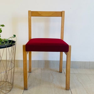May include: A wooden chair with a red upholstered seat. The chair has a simple design with straight lines and a rectangular back.