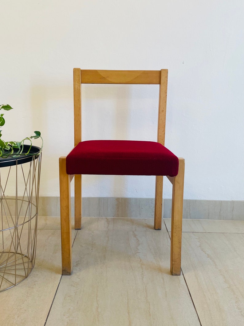 May include: A wooden chair with a red upholstered seat. The chair has a simple design with straight lines and a rectangular back.