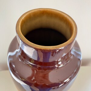 May include: A brown ceramic vase with a glossy finish. The vase has a wide, rounded body that tapers towards the base. The rim is a lighter brown color. The interior is dark brown. The vase is likely used for decorative purposes.