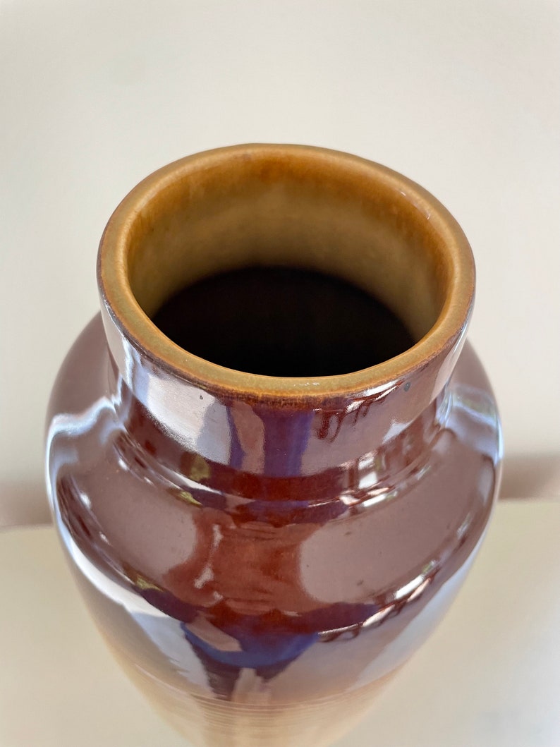 May include: A brown ceramic vase with a glossy finish. The vase has a wide, rounded body that tapers towards the base. The rim is a lighter brown color. The interior is dark brown. The vase is likely used for decorative purposes.