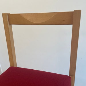 May include: A wooden chair with a red upholstered seat. The chair has a curved back and a simple design.