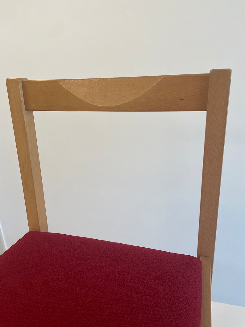 May include: A wooden chair with a red upholstered seat. The chair has a curved back and a simple design.