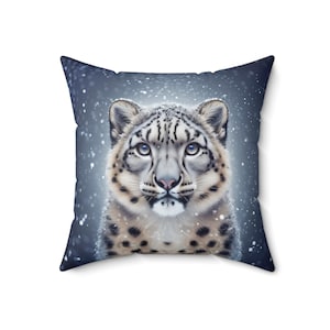 Pode incluir: Uma almofada com um leopardo das neves sobre um fundo azul. O leopardo das neves está olhando diretamente para a câmera com uma pelagem manchada de branco e preto.