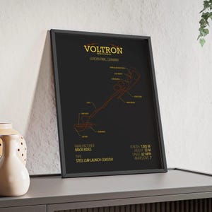 May include: Black framed poster of the Voltron Nevera roller coaster at Europa Park, Germany. The poster displays an orange diagram of the coaster's track, with details including length (1385 m), height (32 m), and speed (62 mph).