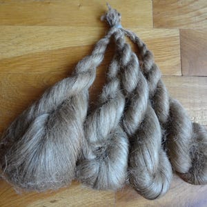 Könnte beinhalten: Ein Bündel hellbraunen, natürlichen Fasergarns, zu Seilen gedreht, bereit zum Spinnen oder Weben.