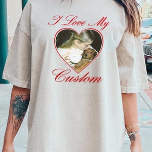 May include: Beige t-shirt with the text "I Love My Custom" in red script. A heart-shaped graphic in the centre features a photo of a person kissing a small brown dog. The shirt has short sleeves and a relaxed fit.