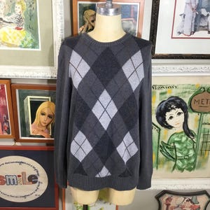 May include: A gray sweater with a diamond pattern in white and gray. The sweater has long sleeves and a crew neck.