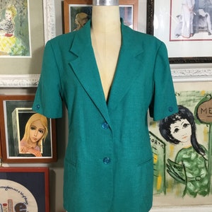 May include: A teal blazer with short sleeves and three buttons. The blazer has a single pocket on the left side.