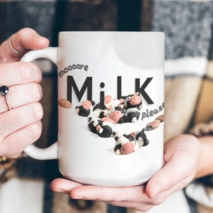 May include: White ceramic mug with a black and white illustration of cows and the text "Moooore Milk Please".