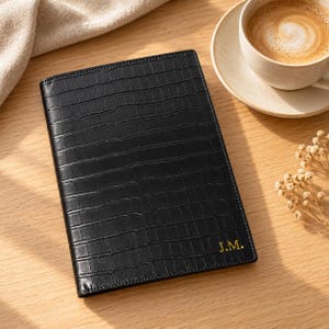 May include: A black rectangular notebook cover featuring a textured crocodile skin pattern and the gold embossed initials J.M. in the bottom right corner. The cover is constructed with stitched edges and has a smooth, glossy finish throughout.