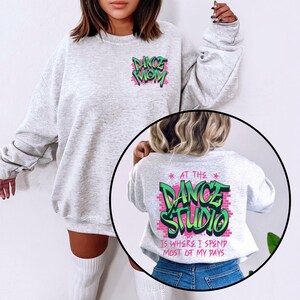 以下が含まれることがあります： グレーのトレーナーにピンクとグリーンの文字で「Dance Mom」と書いてあります。もう一枚のトレーナーにはピンクとグリーンの文字で「At the Dance Studio is where I spend most of my days」と書いてあります。