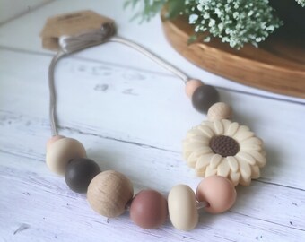 May include: A beige and brown silicone necklace with wooden beads and a sunflower charm. The necklace is made for babies and toddlers.