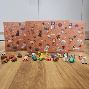 May include: A set of 24 small animal figurines, including a cat, dog, turtle, fish, and more. The figurines are arranged in a row on a wooden surface. The figurines are made of plastic and are brightly coloured.