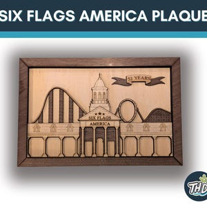 Könnte beinhalten: Holztafel mit einem lasergeschnittenen Design von Six Flags America. Die Tafel zeigt eine Achterbahn, ein Gebäude mit einem Turm und den Text "SIX FLAGS AMERICA PLAQUE" und "51 YEARS". Die Tafel ist in dunklem Holz gerahmt.