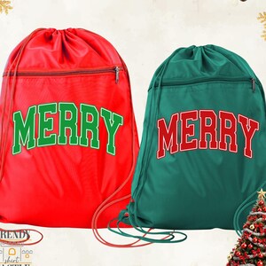 May include: Two drawstring bags, one red and one green, each with the word "MERRY" in bold, outlined letters. The red bag has green lettering, and the green bag has red lettering. Both bags have a zippered pocket and red drawstring cords.