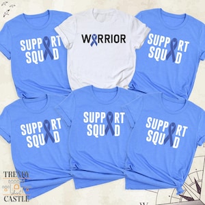 May include: Five light blue t-shirts with white text and a blue ribbon design. The text on the shirts reads "Support Squad" and "Warrior".