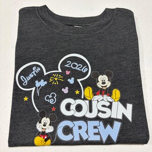 Puede incluir: Camiseta gris oscuro con gr&aacute;ficos de Mickey Mouse y el texto "Cousin Crew". El dise&ntilde;o incluye el nombre "Justin" y el a&ntilde;o "2020" en un dise&ntilde;o de oreja de Mickey Mouse. Tambi&eacute;n aparecen dos personajes de Mickey Mouse.