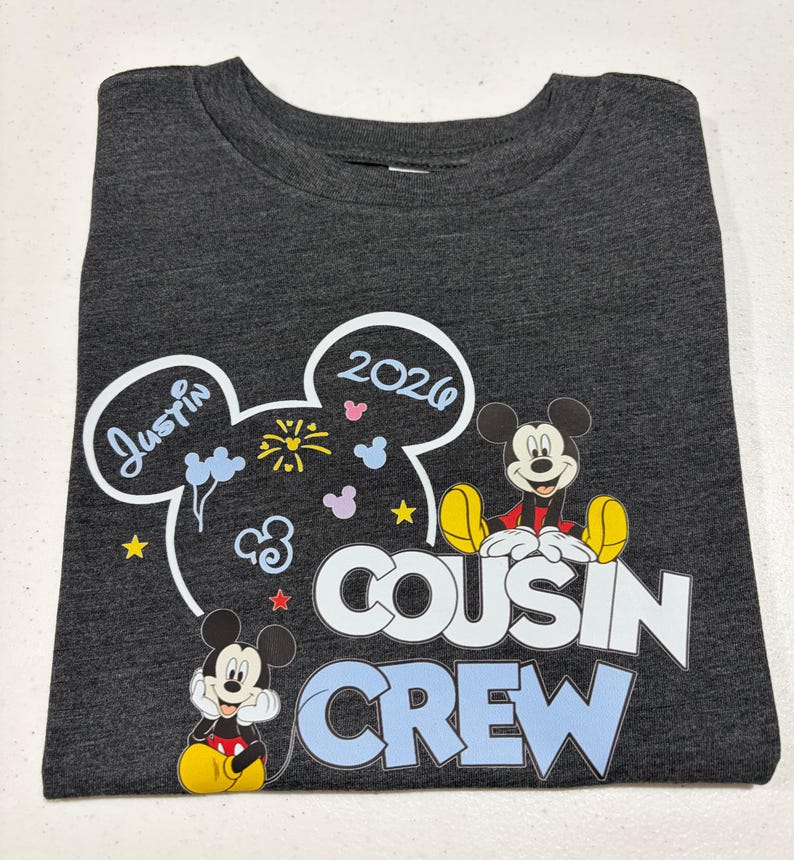 Puede incluir: Camiseta gris oscuro con gr&aacute;ficos de Mickey Mouse y el texto "Cousin Crew". El dise&ntilde;o incluye el nombre "Justin" y el a&ntilde;o "2020" en un dise&ntilde;o de oreja de Mickey Mouse. Tambi&eacute;n aparecen dos personajes de Mickey Mouse.