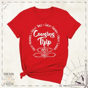 Peut inclure: Un t-shirt rouge vif &agrave; manches courtes avec un graphisme blanc indiquant Cousins Trip, Great Times, Great Friends, Great Laughs, Great Memories, 2026 et PHUKET, accompagn&eacute; d'un c&oelig;ur et de deux illustrations de panneaux directionnels.