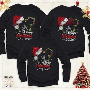 May include: Three black long-sleeve shirts featuring a graphic of a red Santa hat and green dots forming Mickey Mouse ears above a white castle silhouette. The text reads Disney Christmas 2026 in red and white lettering with small white snowflakes.