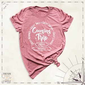 Peut inclure: Un t-shirt &agrave; manches courtes rose poudr&eacute; avec du texte blanc indiquant Cousins Trip, Great Times, Great Friends, Great Memories, Great Laughs, 2026 et Nashville, accompagn&eacute; d'un graphique repr&eacute;sentant deux panneaux directionnels et un c&oelig;ur.