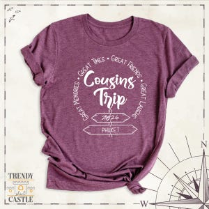 Peut inclure: Un t-shirt &agrave; manches courtes bordeaux chin&eacute; avec un texte blanc indiquant Cousins Trip, 2026 et Phuket, entour&eacute; des phrases Great Times, Great Friends, Great Laughs et Great Memories dispos&eacute;es dans un motif circulaire.