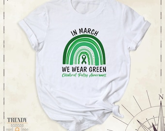 May include: A white short-sleeved t-shirt featuring a green rainbow graphic with a central awareness ribbon. The text reads IN MARCH WE WEAR GREEN and Cerebral Palsy Awareness in black and green lettering centered on the chest area.
