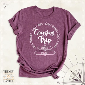 Peut inclure: Un t-shirt &agrave; manches courtes bordeaux chin&eacute; avec un texte blanc indiquant Cousins Trip, 2026 et Phuket, entour&eacute; des phrases Great Times, Great Friends, Great Laughs et Great Memories dispos&eacute;es dans un motif circulaire.