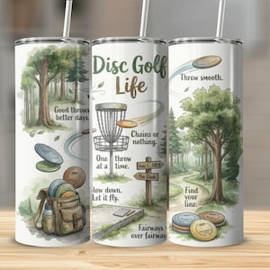 May include: A white tumbler with a watercolor design featuring disc golf elements. The design includes trees, a disc golf basket, discs, and text that reads "Disc Golf Life." The tumbler has a straw and is designed for cold beverages.