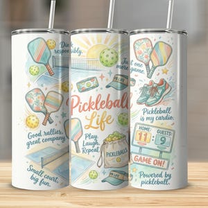May include: A white tumbler with a colourful Pickleball Life design. The design includes pickleball paddles, balls, nets, and the text "Pickleball Life." The tumbler has a straw and is decorated with the phrases "Good rallies, great company" and "Pickleball is my cardio."