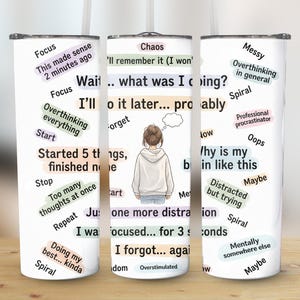 May include: A white tumbler with a humorous design. The tumbler features a cartoon illustration of a person and text bubbles with phrases like "Focus," "Overthinking," and "Chaos." The tumbler is designed to hold beverages.