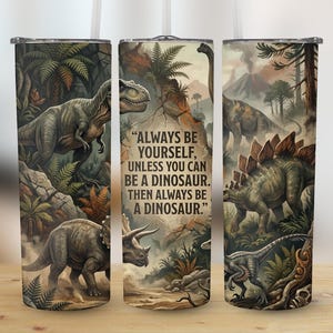 Può includere: Bicchiere con un'illustrazione dettagliata di vari dinosauri in un paesaggio preistorico. Il design include un Tyrannosaurus Rex, uno Stegosauro e un Triceratopo, con il testo "ALWAYS BE YOURSELF, UNLESS YOU CAN BE A DINOSAUR. THEN ALWAYS BE A DINOSAUR."