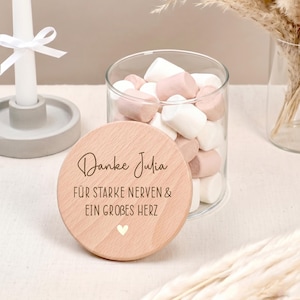 Könnte beinhalten: Ein klares Glas mit rosa und weißen Marshmallows, bedeckt mit einem hellen Holzdeckel. Der Deckel ist mit den Worten "Danke Julia" und anderem deutschen Text sowie einem kleinen Herzen graviert. Das Glas steht auf einer weißen Oberfläche.