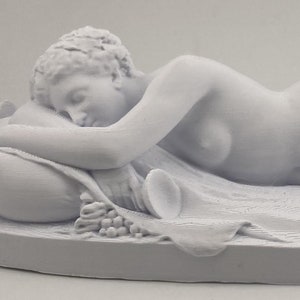 May include: A white sculpture of a reclining figure, possibly a classical depiction. The figure is lying on a draped surface, with one arm resting on a pillow. The sculpture includes details such as hair, facial features, and drapery.