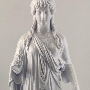 Może przedstawiać: Biała, pomalowana statua kobiety w płynnej szacie, stojąca na kwadratowej podstawie.