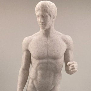 May include: A white marble statue of a nude male figure standing with one leg slightly forward. The statue is detailed with a textured surface and is on a square base.