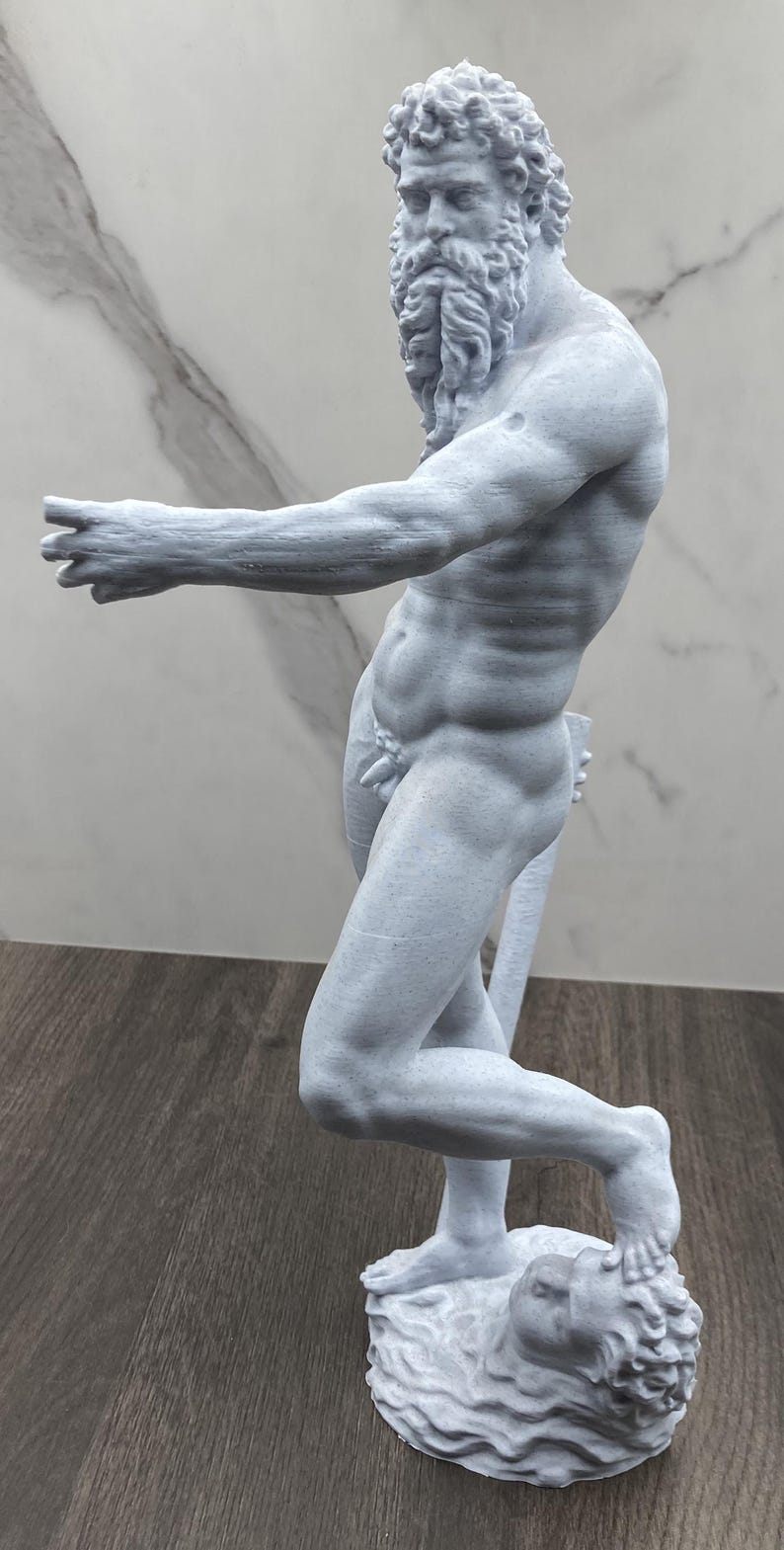 Puede incluir: Estatua gris claro de una figura masculina musculosa con barba larga y cabello rizado. La estatua est&aacute; sobre una base con un rostro esculpido. El brazo de la figura est&aacute; extendido y la estatua est&aacute; detallada con musculatura visible.