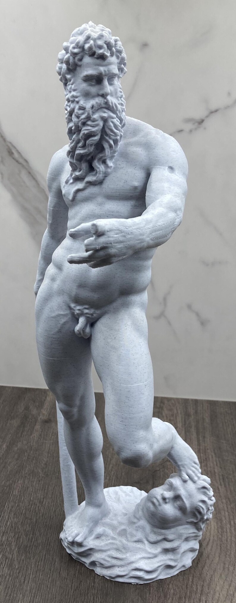 Puede incluir: Estatua gris claro de una figura masculina musculosa con barba larga y cabello rizado. La estatua est&aacute; en una pose din&aacute;mica, con una pierna doblada y la otra descansando sobre una cabeza esculpida. La mano de la figura est&aacute; extendida.