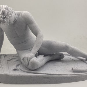 Puede incluir: Una escultura blanca y detallada de una figura masculina desnuda tumbada sobre una base circular. La figura está representada en una pose reclinada, con un brazo apoyado en la base y la otra mano cerca de la rodilla.
